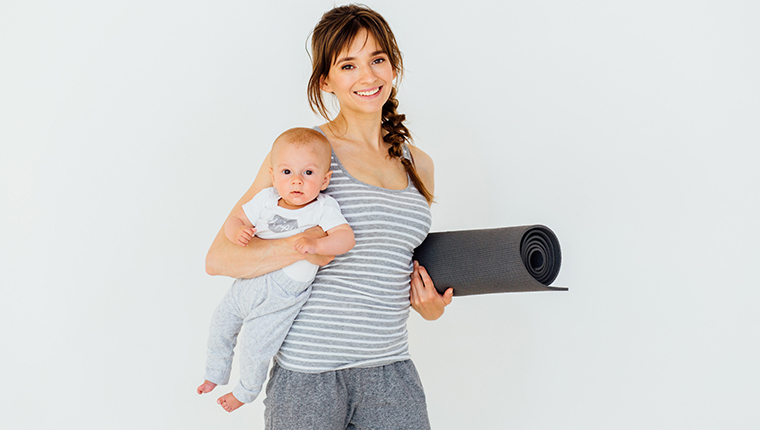 mor smiler og holder baby og sammenrullet yogamaatte