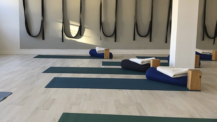 Ananda Yoga - yogalokale med måtter udstyr og remme på væg i baggrund